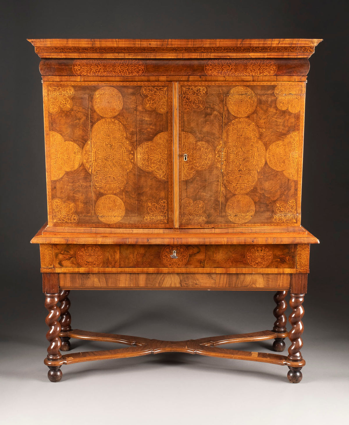 An ornate walnut cabinet with geometric marquetry, featuring Baroque style legs and two doors.